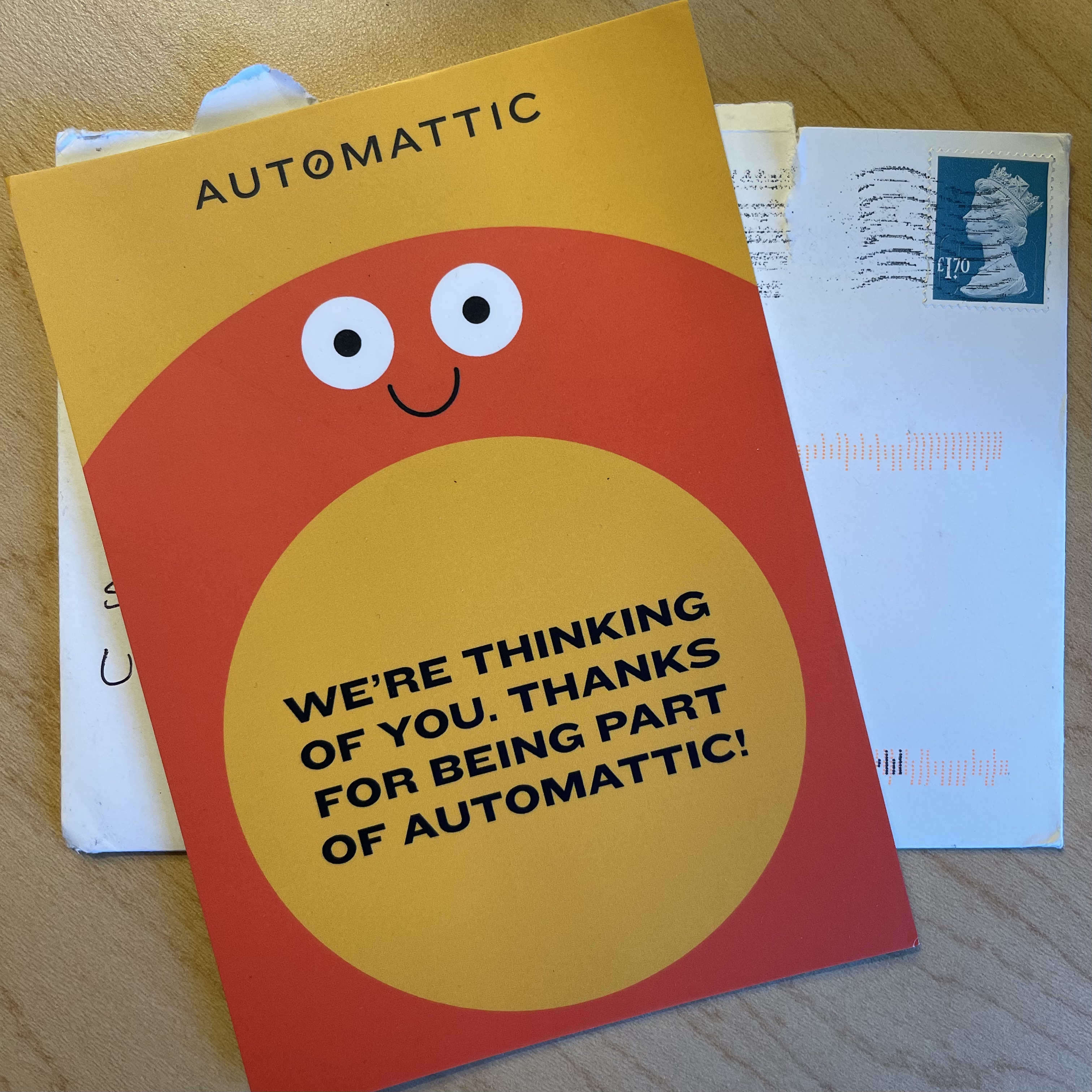 Photograph of a card and envelope I got with a canceled stamp. The card reads "We're thinking of you. Thanks for being a part of Automattic!". There's a smiley face on it as well.